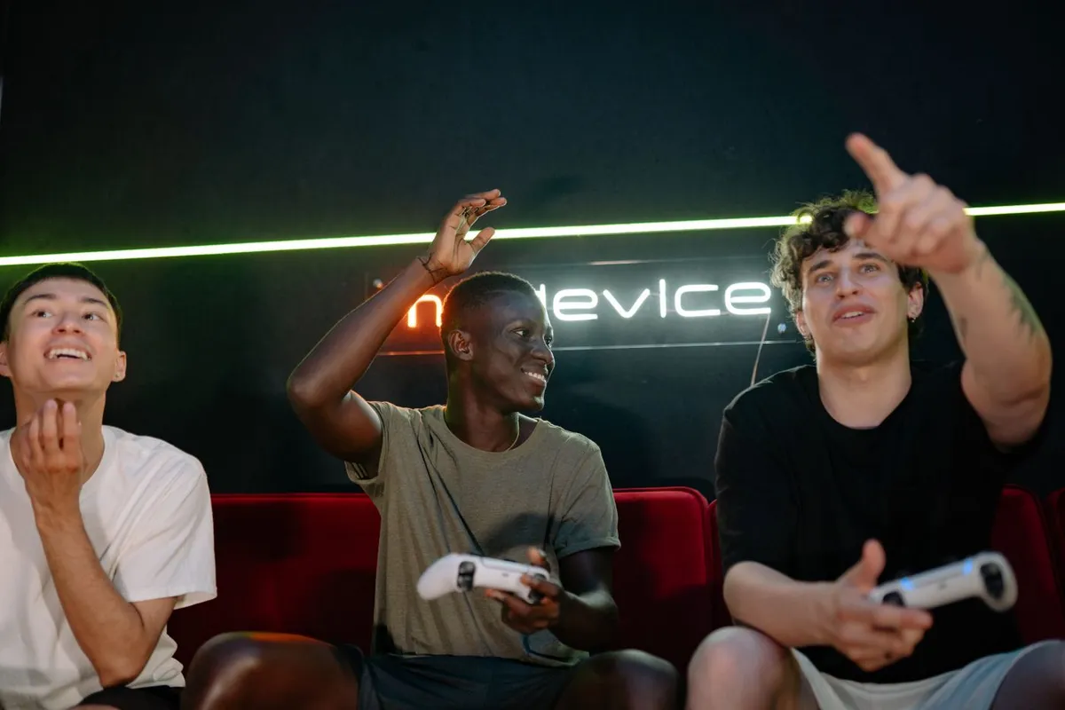 Three young adult friends laughing and playing console games together on a couch